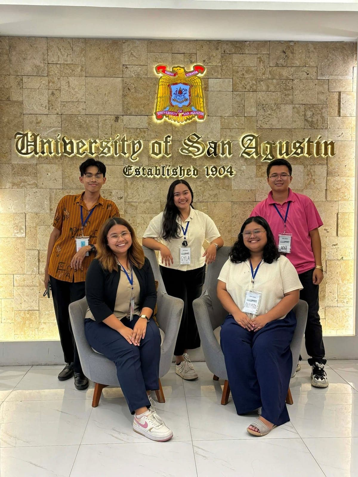 The teachers wearing training IDs beneath the University of San Agustin lobby sign