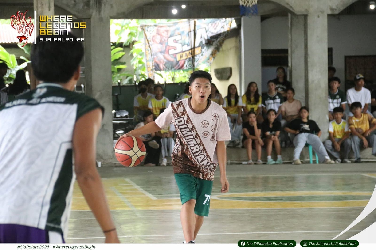 A Dimitrians player brings the ball up the court during a basketball game, watched by seated students in house colors